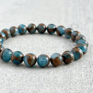 Könnte beinhalten: Ein blaues und braunes Edelstein-Armband mit runden Perlen. Die Perlen haben ein marmoriertes Muster in Blau und Braun.