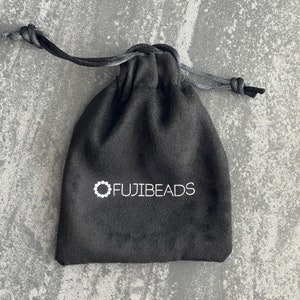Puede incluir: Una bolsa de cord&oacute;n de terciopelo negro con el texto blanco "FUJIBEADS" impreso en la parte delantera.