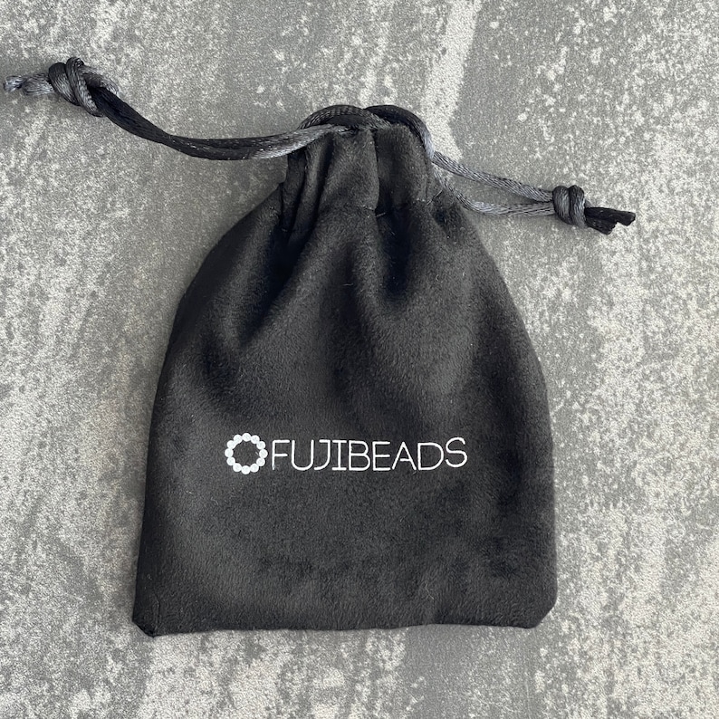 Puede incluir: Una bolsa de cord&oacute;n de terciopelo negro con el texto blanco "FUJIBEADS" impreso en la parte delantera.