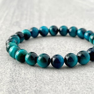 May include: A teal blue tiger's eye beaded bracelet. The beads are round and smooth, and the bracelet is made of natural stone.