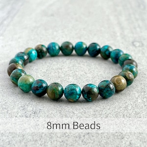 Puede incluir: Un brazalete hecho con cuentas de turquesa de 8 mm. Las cuentas son una mezcla de verde y azul con vetas marrones y blancas.