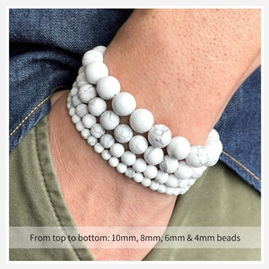 Puede incluir: Cuatro pulseras de cuentas de howlite blancas apiladas en la mu&ntilde;eca de una persona. De arriba a abajo, las cuentas miden 10 mm, 8 mm, 6 mm y 4 mm.
