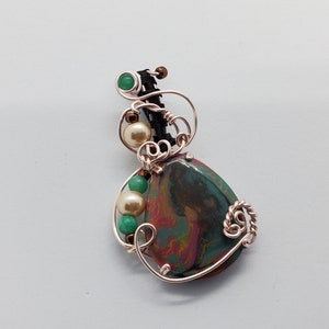 May include: A copper wire wrapped pendant featuring a teardrop-shaped, multi-colored stone with swirls of red, green, and brown. The stone is surrounded by copper wire and accented with small green and white beads.