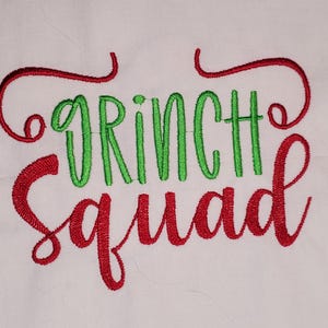 May include: White fabric embroidered with the words "GRINCH SQUAD" in green and red thread. The word "GRINCH" is in green, and "SQUAD" is in red. The design has a festive, holiday theme.