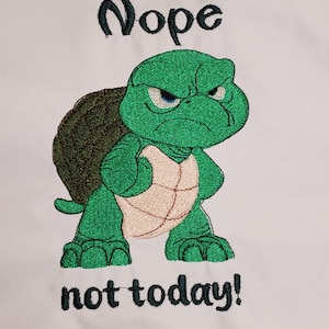 Puede incluir: Diseño bordado de una tortuga verde enfadada con el texto "Nope not today!" sobre un fondo blanco. La tortuga tiene un caparazón marrón y un vientre beige. El texto es de color verde oscuro.