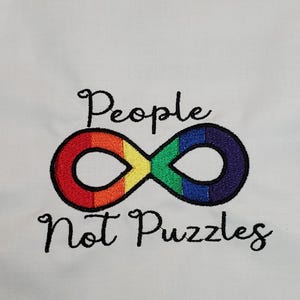 May include: White fabric with embroidered text and a rainbow-colored infinity symbol. The text reads "People Not Puzzles" in black script, with the infinity symbol featuring red, orange, yellow, green, blue, and purple colors.