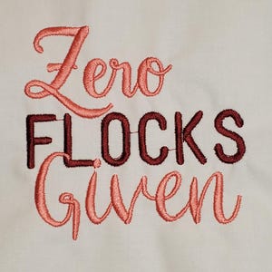 Puede incluir: Texto bordado sobre un fondo blanco que dice "Zero F*cks Given". Las palabras están en una mezcla de cursiva y letras de bloque, con las palabras "Zero" y "Given" en color coral y "F*cks" en rojo oscuro.
