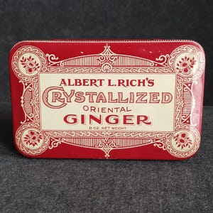 May include: A rectangular red tin with a cream-colored label. The label reads "Albert L. Rich's Crystallized Oriental Ginger" in a decorative font. The tin is 8 oz. net weight.