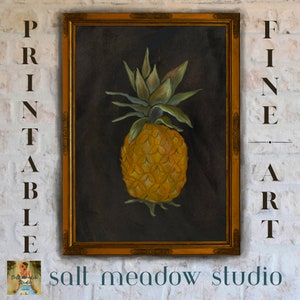 Op de afbeelding: Een schilderij van een ananas in een gouden lijst. De ananas is geel en groen en is geplaatst tegen een donkere achtergrond. Het schilderij is getiteld "salt meadow studio".