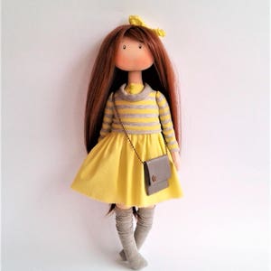 May include: A handmade doll with long brown hair, wearing a yellow dress with grey stripes, grey tights, and a grey purse.