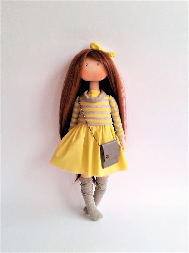 May include: A handmade doll with long brown hair, wearing a yellow dress with grey stripes, grey tights, and a grey purse.