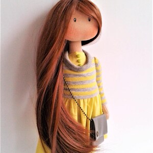 May include: A handmade doll with long brown hair, wearing a yellow and gray striped dress with a yellow skirt and a brown purse. The doll has a yellow flower headband.