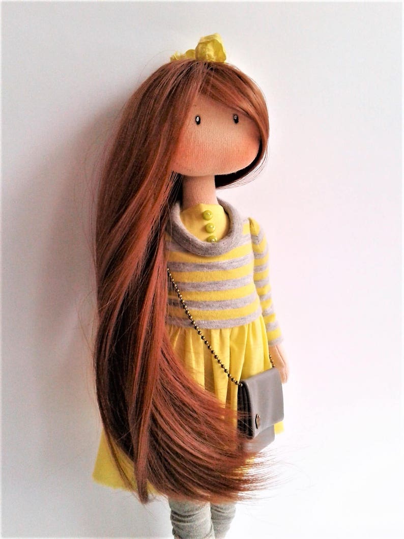 May include: A handmade doll with long brown hair, wearing a yellow and gray striped dress with a yellow skirt and a brown purse. The doll has a yellow flower headband.