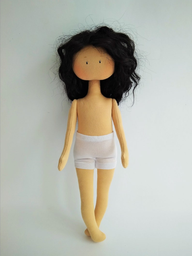 May include: A handmade doll with long black curly hair, a beige body, and white underwear. The doll is standing on a white background.