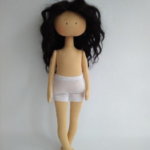 May include: A handmade doll with long black curly hair, a beige body, and white underwear. The doll has a simple face with brown eyes.