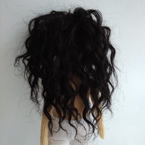 May include: A handmade doll with long, curly black hair and a white fabric skirt. The doll is standing on a white background.