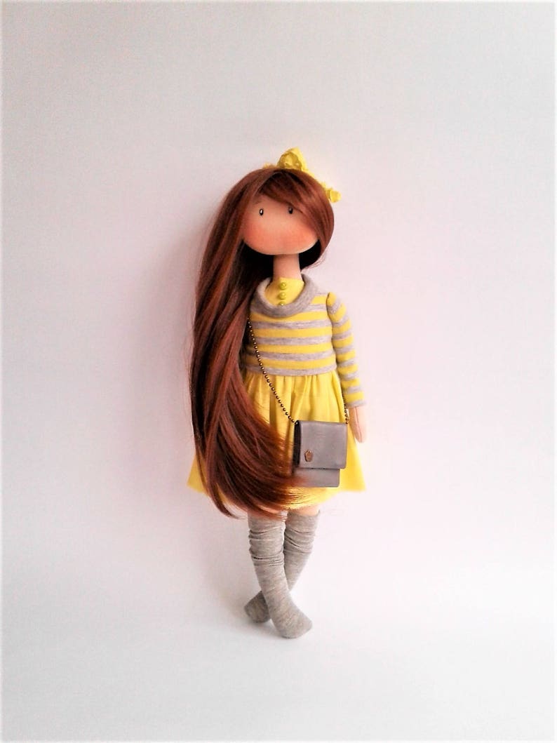 May include: A handmade doll with long brown hair, wearing a yellow and gray striped shirt, a yellow skirt, gray knee-high socks, and a small gray purse.