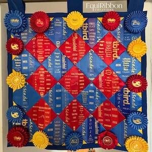 May include: A blue, red, and yellow ribbon quilt with rosettes. The quilt features diamond patterns and ribbons with text like "First Place" and "Horse Show". Rosettes in blue, red, and yellow are attached around the edges.