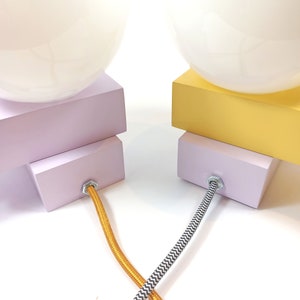 May include: Two table lamps with white globe shades, one with a lavender base and the other with a yellow base. The lamps have black and white patterned cords and gold cords.