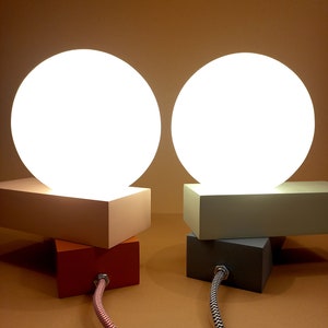 May include: Two white globe lamps with a white, gray, and orange base. The lamps are on a brown surface and have black and white cords.