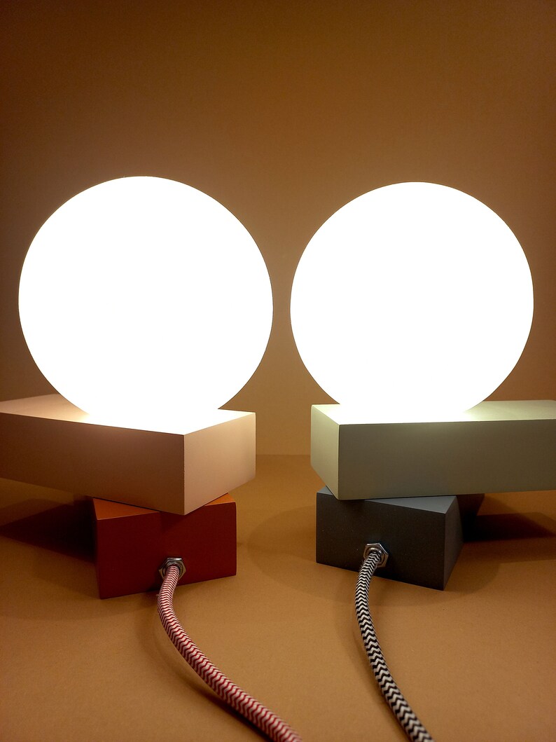 May include: Two white globe lamps with a white, gray, and orange base. The lamps are on a brown surface and have black and white cords.