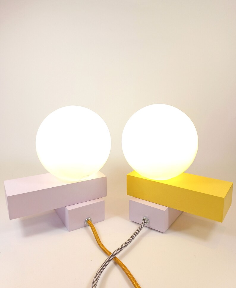 May include: Two table lamps with white globe shades. The lamp on the left has a lavender base and the lamp on the right has a yellow base.