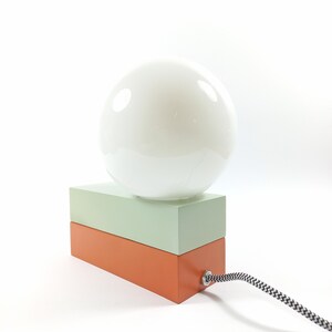 May include: A table lamp with a white globe shade and a two-toned base. The base is made of wood and is painted in shades of green and orange.