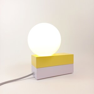May include: A yellow and white table lamp with a round white shade. The lamp has a cord with a black and white pattern.