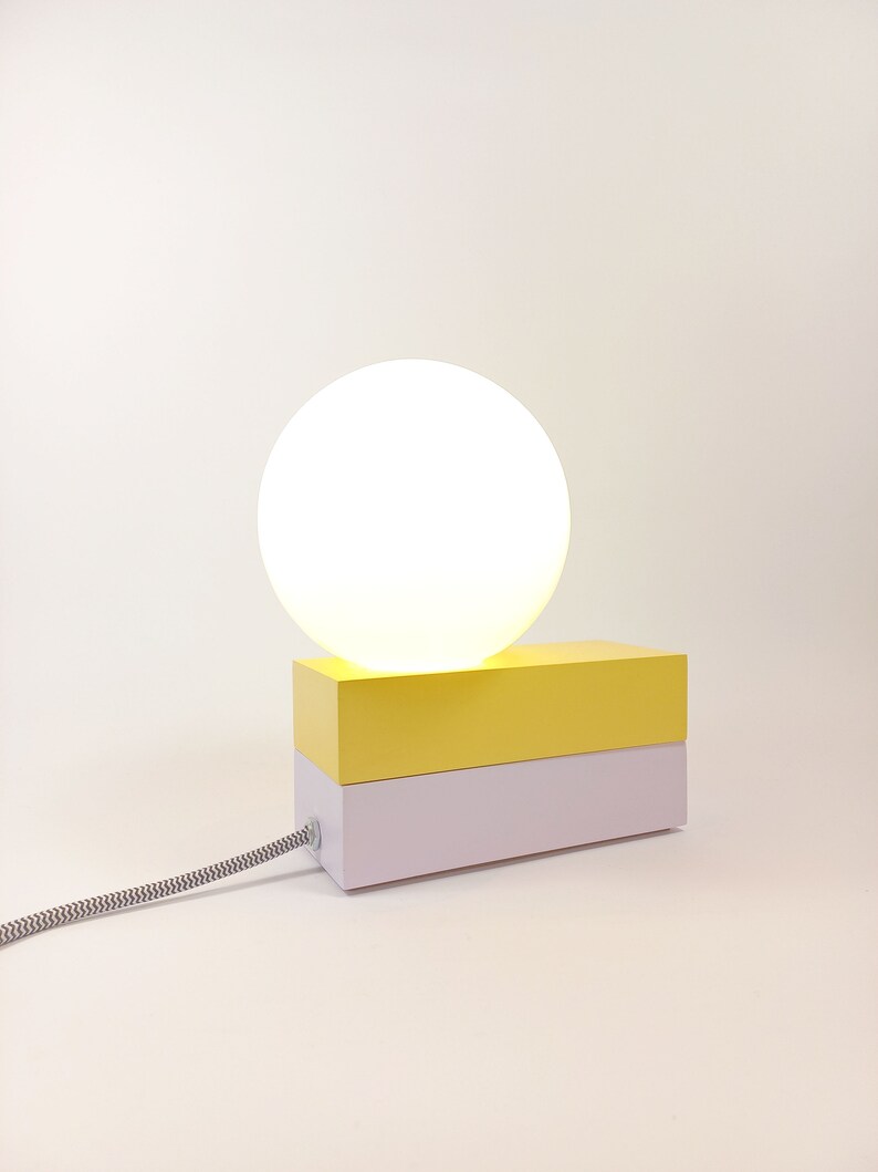 May include: A yellow and white table lamp with a round white shade. The lamp has a cord with a black and white pattern.