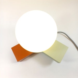 May include: A white globe lamp with a light orange and light green base. The lamp is on a white surface.