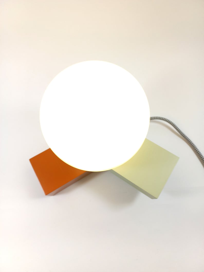 May include: A white globe lamp with a light orange and light green base. The lamp is on a white surface.