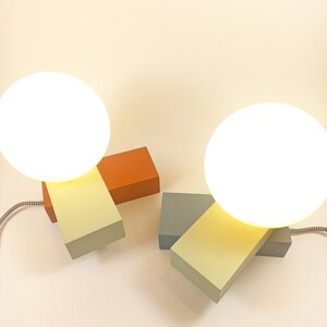 May include: Two modern table lamps with white globe shades. The lamps are made of wood blocks in orange, light green, and gray.