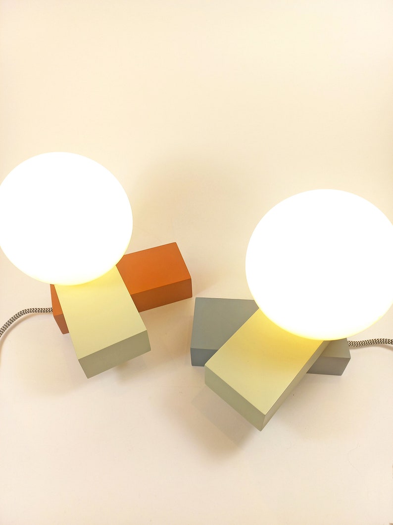 May include: Two modern table lamps with white globe shades. The lamps are made of wood blocks in orange, light green, and gray.