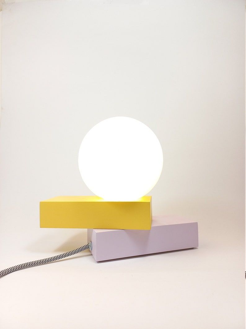 May include: A modern table lamp with a white globe shade and a yellow and purple base.