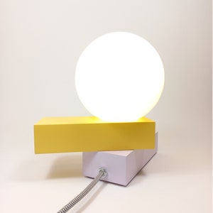 May include: A yellow and white table lamp with a round white shade. The lamp has a black and white cord.