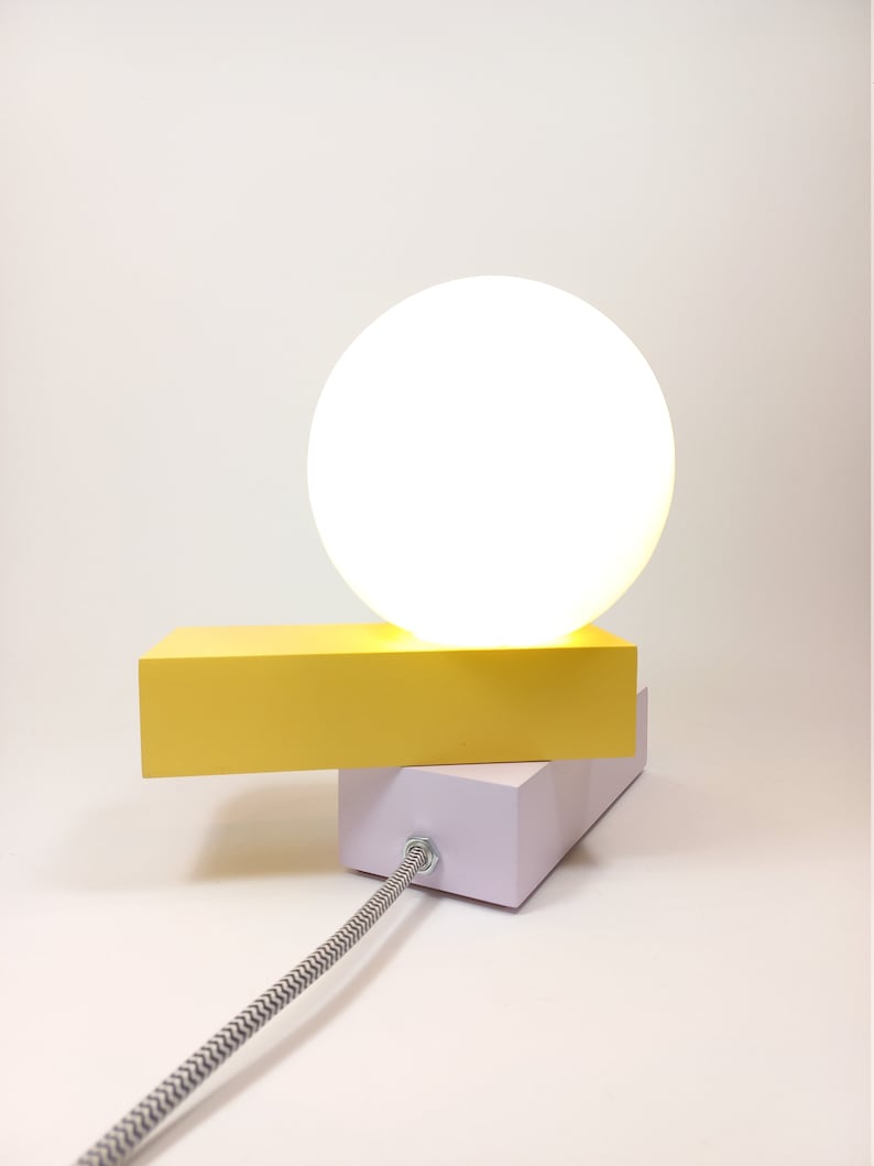 May include: A yellow and white table lamp with a round white shade. The lamp has a black and white cord.