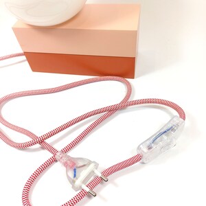 May include: A white globe lamp with a red and white striped cord and a clear inline switch. The lamp sits on a two-tiered base, the top tier is light pink and the bottom tier is orange.