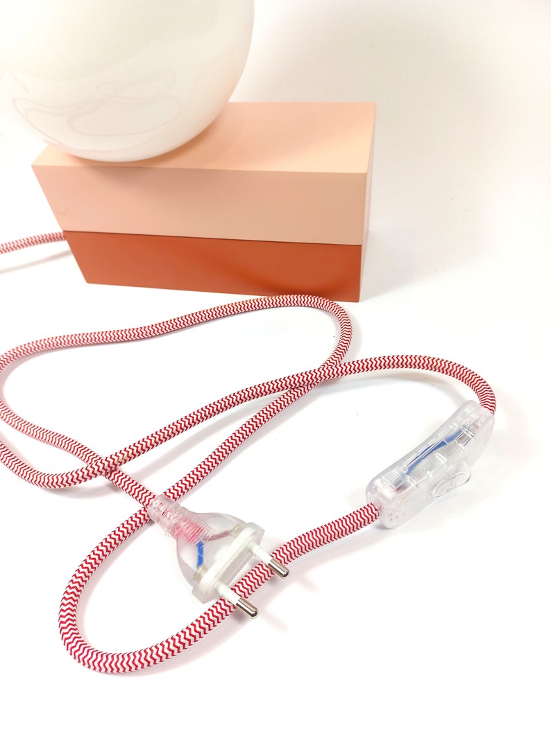 May include: A white globe lamp with a red and white striped cord and a clear inline switch. The lamp sits on a two-tiered base, the top tier is light pink and the bottom tier is orange.