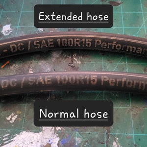 May include: Two black hoses with white text. The top hose is labeled "752-DC / SAE 100R15 Performance" and is extended. The bottom hose is labeled "762-DC/SAE 100R15 Performance" and is in its normal state.