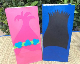 May include: Two party favor bags decorated with characters from the Trolls movie. One bag is pink with a pink troll with blue and green hair. The other bag is blue with a blue troll with black hair.