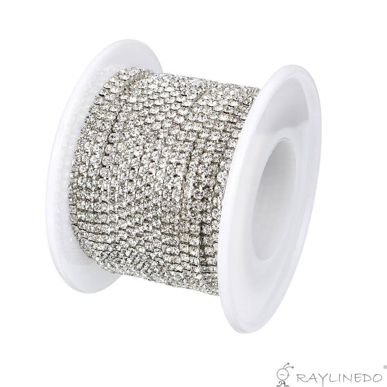 May include: A spool of silver rhinestone chain. The chain is tightly wound on a white plastic spool. The rhinestones are small and closely set, creating a continuous, sparkling line. The chain is ideal for jewelry making and craft projects.