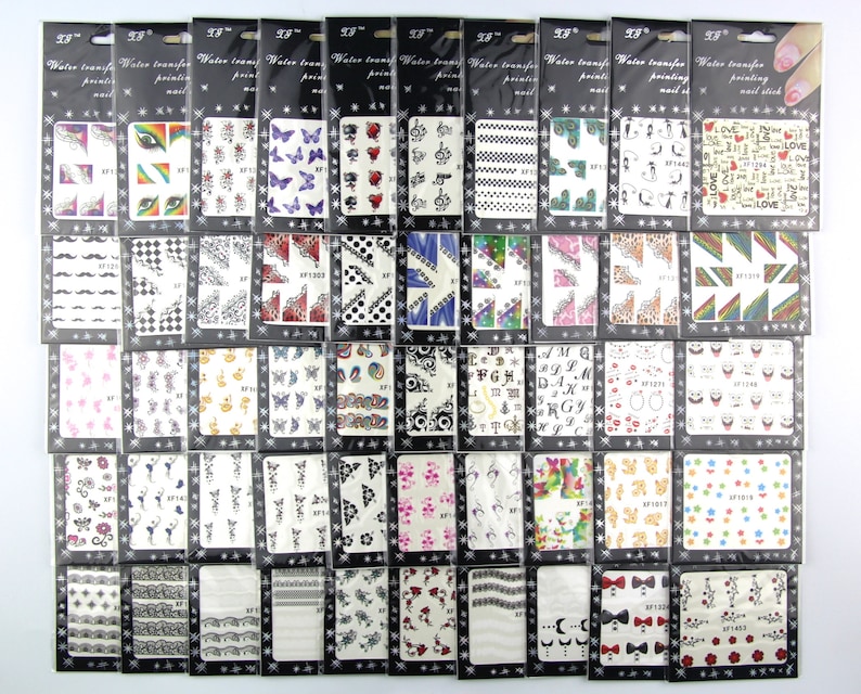 May include: A set of 48 water transfer nail art stickers. The stickers are packaged in individual clear plastic bags with black borders. Each bag features a different design, including butterflies, musical notes, hearts, stars, and geometric patterns.