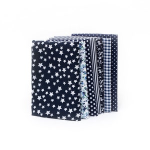 May include: A stack of fabric bundles in various patterns, including white stars on navy, floral, polka dots, stripes, and gingham. The fabrics are arranged vertically against a white background, showcasing a range of textile designs.
