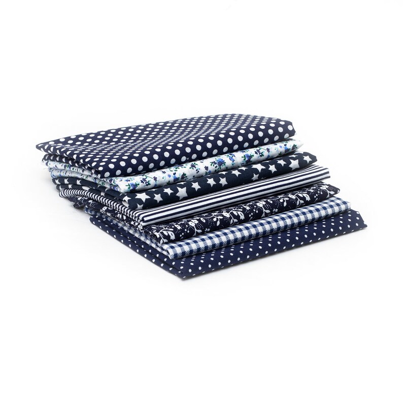 K&ouml;nnte beinhalten: Ein Stapel gefalteter Stoffst&uuml;cke mit verschiedenen Mustern. Die Stoffe weisen Designs wie wei&szlig;e Punkte auf Marineblau, Blumendrucke, Sterne, Streifen und Vichy-Karo auf. Die Stoffe sind wahrscheinlich aus Baumwolle oder einem &auml;hnlichen Material, geeignet f&uuml;r N&auml;hprojekte.