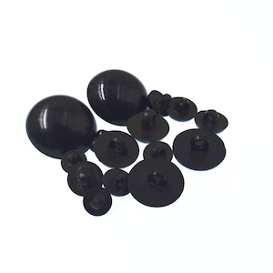 May include: A collection of black plastic buttons, including two large round buttons and several smaller flat buttons with a hole in the center.