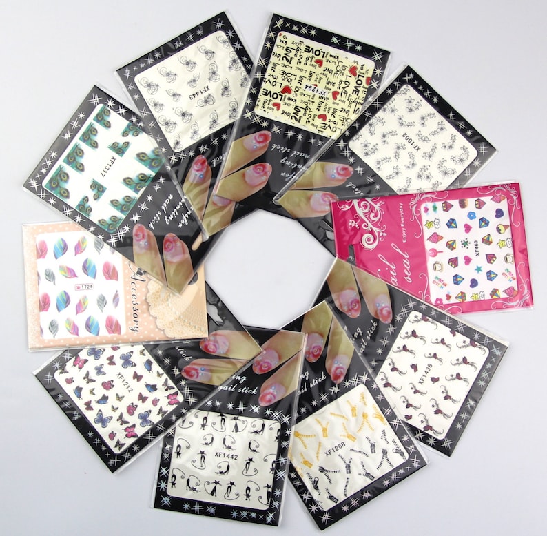 May include: Assortment of nail art stickers in various designs, including butterflies, peacocks, leaves, and hearts. The stickers are packaged in clear plastic bags with black borders and white text.