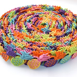 Op de afbeelding: Een rol kleurrijke ananasvormige trim, perfect om een tropische touch toe te voegen aan knutselwerk en kleding. De trim is gemaakt van een zachte, textuurrijke stof en heeft een verscheidenheid aan felle kleuren, waaronder roze, oranje, geel, groen en paars.