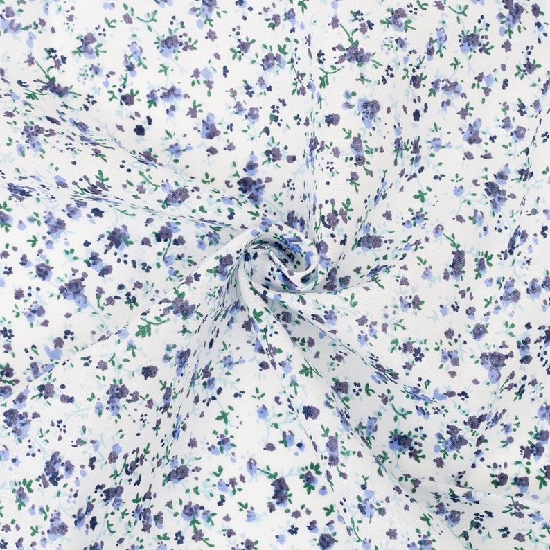 K&ouml;nnte beinhalten: Wei&szlig;er Stoff mit einem zarten Blumenmuster. Das Design zeigt kleine, verstreute blaue und violette Blumen mit gr&uuml;nen Bl&auml;ttern. Der Stoff ist dicht gewebt und scheint aus Baumwolle oder einem &auml;hnlichen Material zu bestehen, geeignet f&uuml;r N&auml;hprojekte.