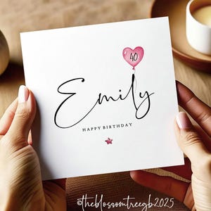 May include: A white card with a pink heart balloon with the number 40 inside. The name Emily is written in cursive script with the words Happy Birthday underneath. A small pink star is below the text. The card has the text @theblossomtreegb2025 in the bottom right corner.