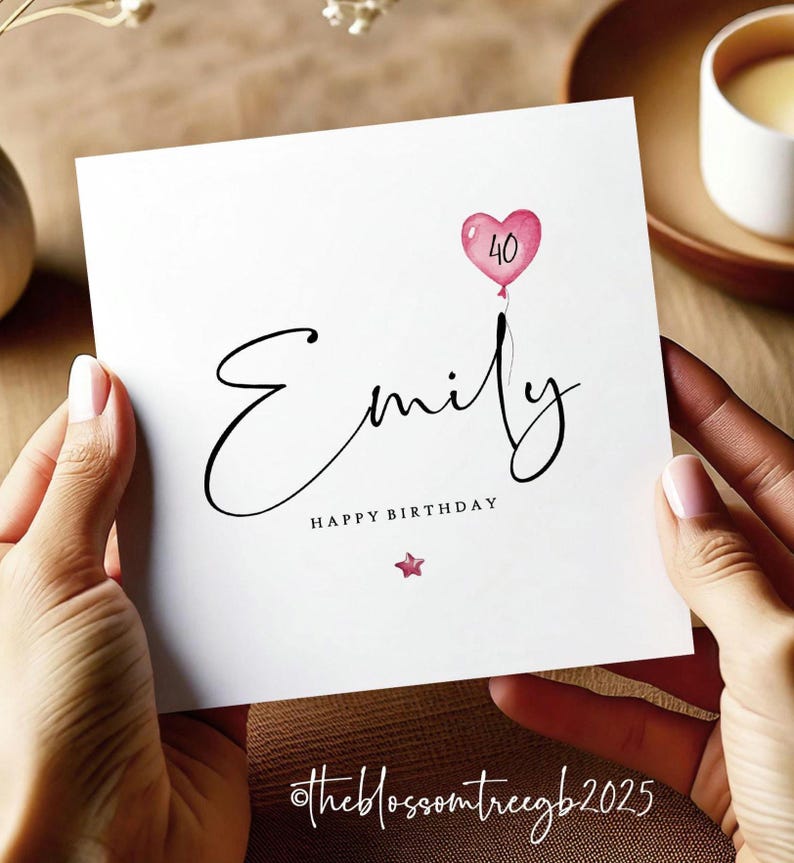 May include: A white card with a pink heart balloon with the number 40 inside. The name Emily is written in cursive script with the words Happy Birthday underneath. A small pink star is below the text. The card has the text @theblossomtreegb2025 in the bottom right corner.
